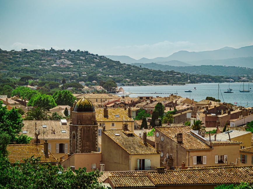 Scenic view of a coastal town in Southern France with rooftops, hills, and the sea.