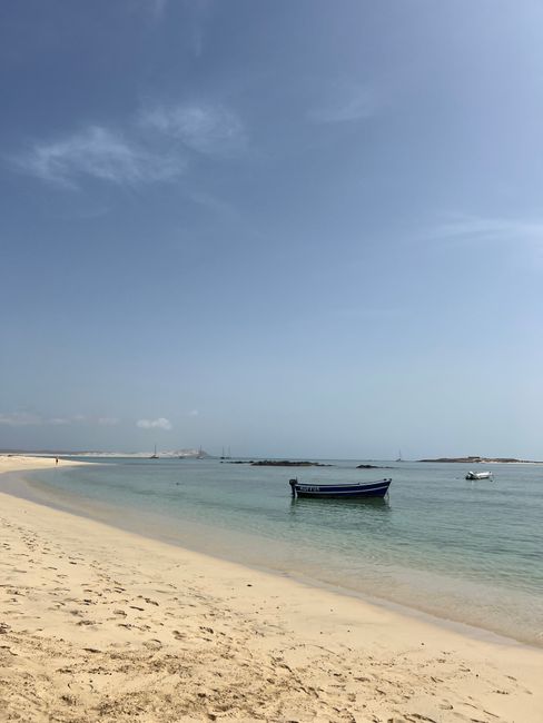 Peaceful beach scene in Sal Rei, Cabo Verde, with a boat on turquoise water and clear skies.