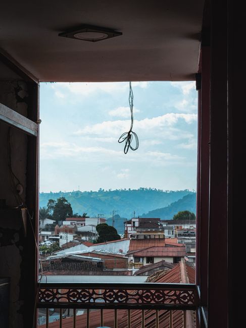 A picturesque view of rooftops and mountains in Salento, Colombia, framed by a window.