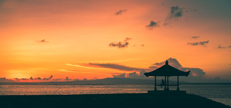 A picturesque sunset in Bali featuring an ocean view with a silhouette of a gazebo.