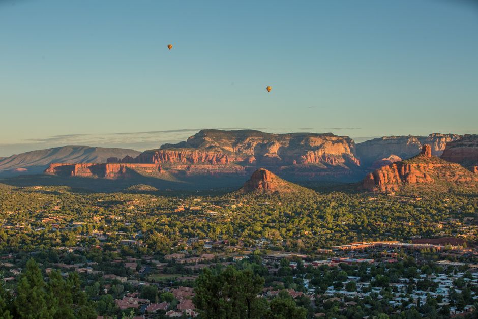Breathtaking view of Sedona's red rock formations at sunset with hot air balloons in the sky.