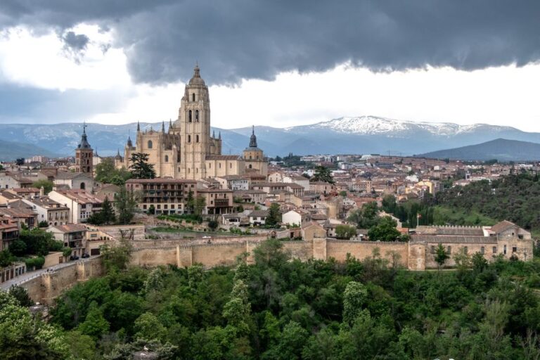 Panoramic view of Segovia Cathedral with lush greenery and historical architecture under dramatic clouds.