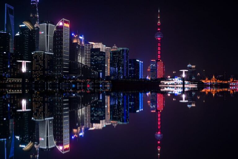 Dazzling night view of Shanghai's Pudong skyline with the iconic Oriental Pearl Tower reflecting on the water.