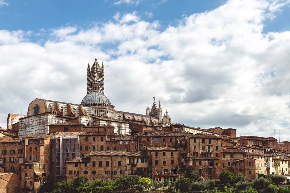 A scenic view of Siena's historic cityscape featuring the iconic Siena Cathedral under a cloudy sky in Tuscany, Italy.