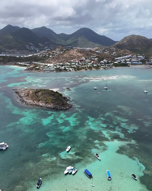 A stunning aerial photograph of Saint Martin's turquoise waters, islands, and boats, showcasing the serene coastal beauty.