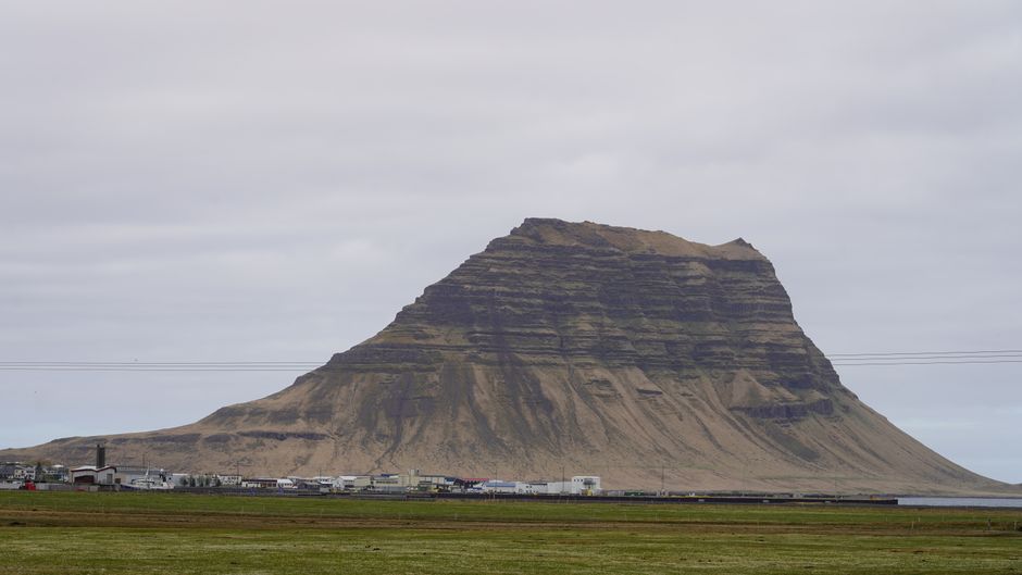 Stunning view of Kirkjufell Mountain under a cloudy sky in Iceland, highlighting its unique shape and the surrounding landscape.