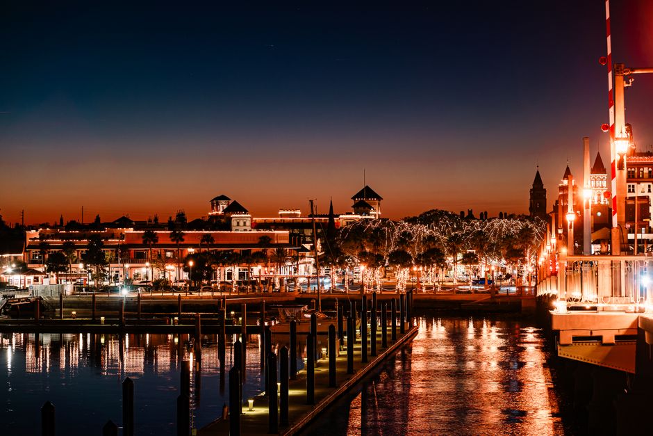 Beautiful nighttime view of St. Augustine Harbor, Florida, with lit buildings and boats reflecting on the water.