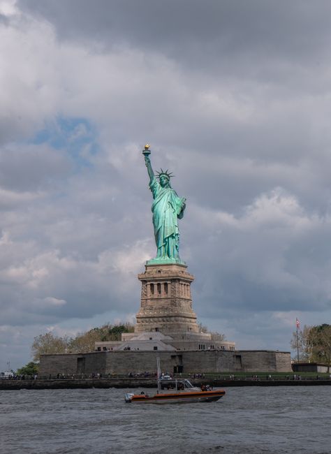Iconic Statue of Liberty with a boat passing by under cloudy skies in New York City.