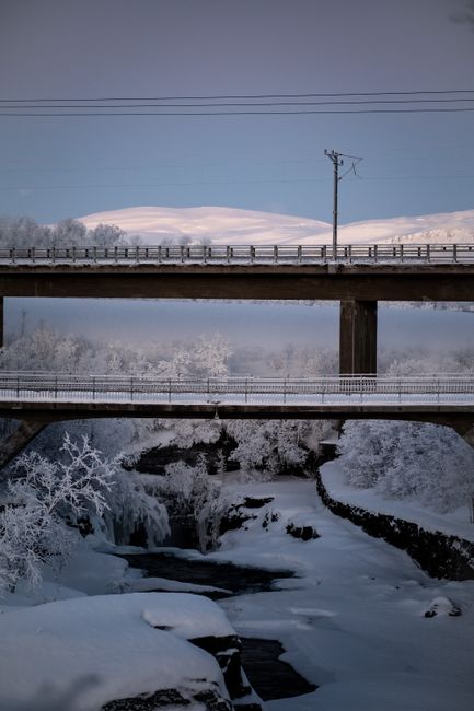 Two snow-covered bridges over a frozen river in Abisko, Sweden, during winter.