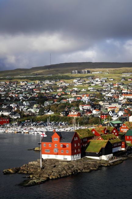 Picturesque coastal village in Faroe Islands showcasing traditional red and turf-roofed houses, embraced by serene landscape.