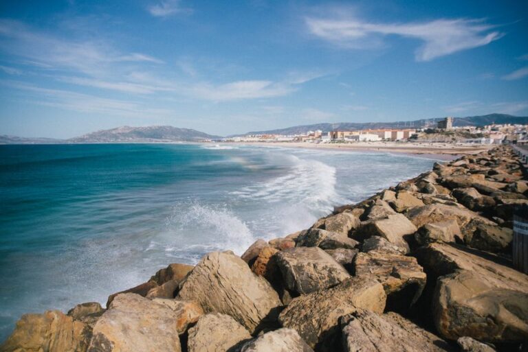 Picturesque scenery of turquoise bay of sea washing rocky coast against blue sky with rare clouds near small town on sunny day