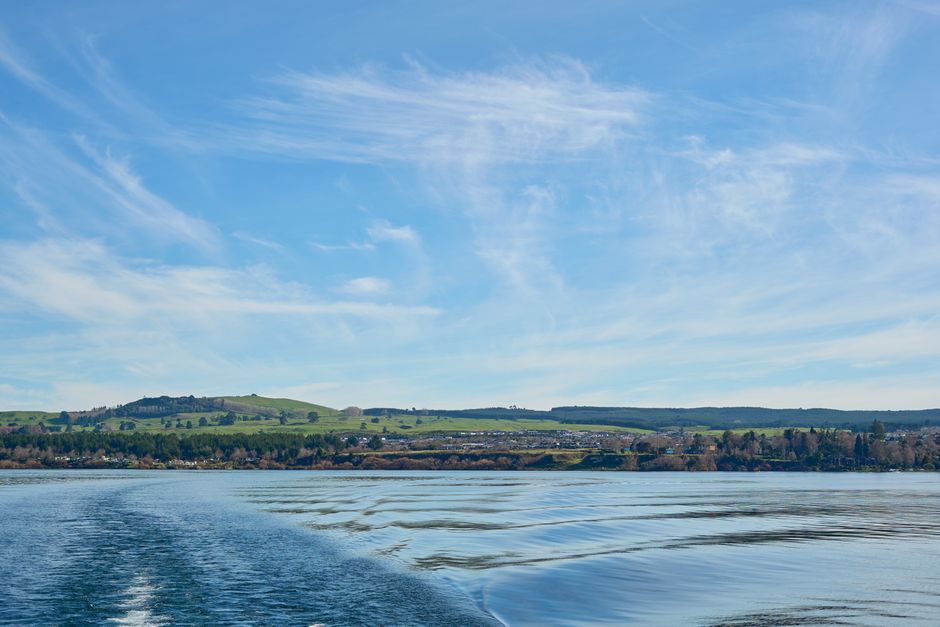 Tranquil summer scene of Lake Taupō, New Zealand, with rolling hills and a vivid blue sky.