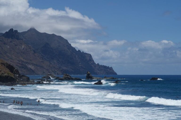 Captivating view of Benijo coast with waves crashing on rocky shore under blue skies.