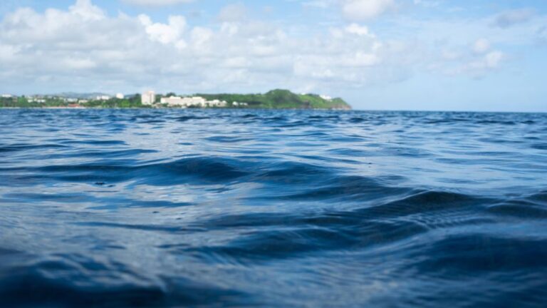 Serene ocean scene with Tumon Bay in the background, showcasing clear blue waters and sky.