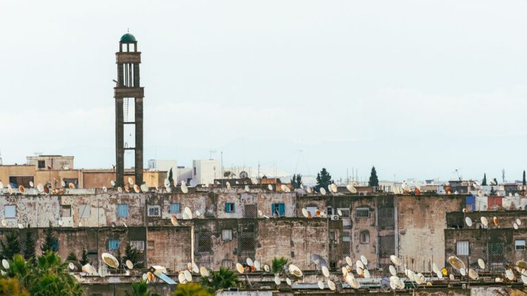 Urban rooftops with satellite dishes beneath a towering minaret in Tunis, Tunisia.