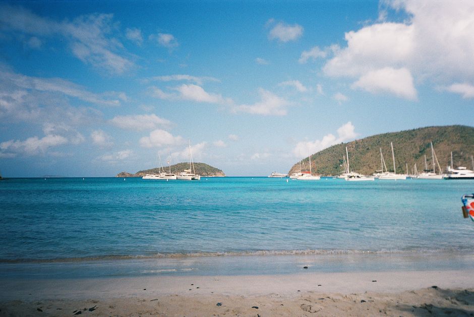 Beautiful Caribbean beach scene with sailboats and islands in the background on a sunny day.