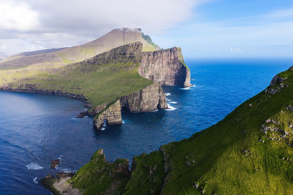 A breathtaking aerial shot of lush green cliffs and blue ocean in Faroe Islands, showcasing natural beauty.