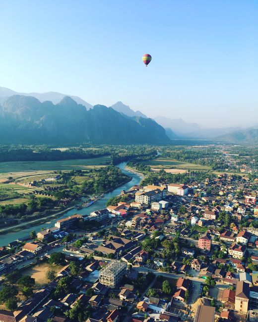 Discover the breathtaking aerial view of Vang Vieng, Laos, with a hot air balloon soaring above the town.
