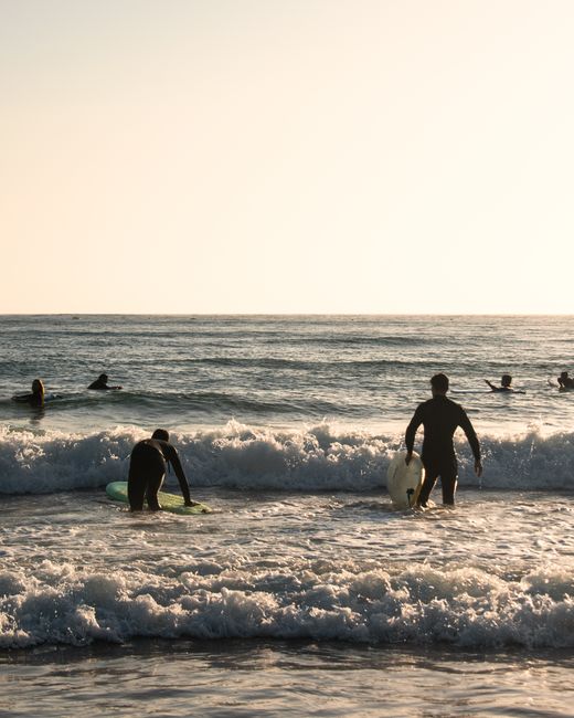 Surfers in wetsuits catching waves at Aljezur Beach, Portugal, during sunset.