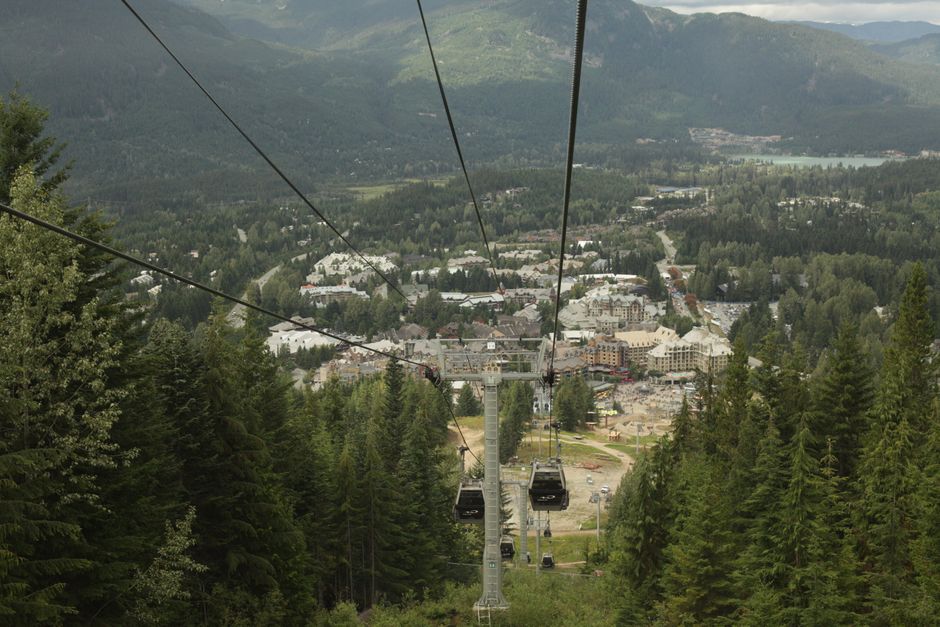 Aerial view of cable cars over lush forest with mountains and town in background.