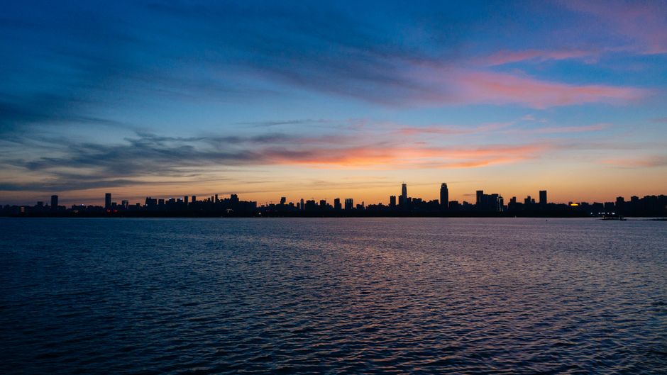 The serene skyline of Wuhan silhouetted against a twilight sky over a calm river.