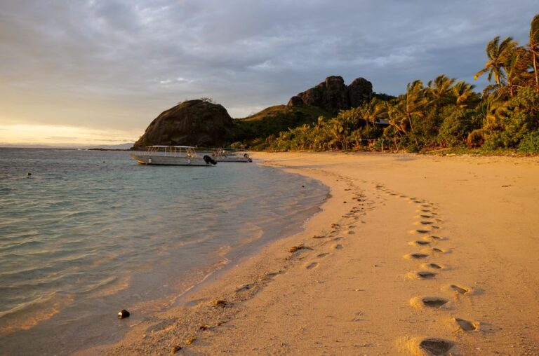 Beautiful beach view of Yasawa Islands, Fiji, at sunset with footprints and boats.