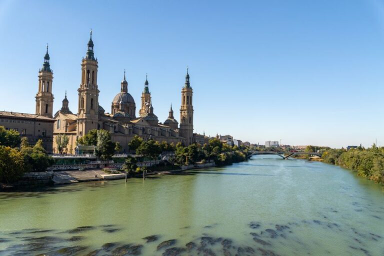 Stunning view of Basilica del Pilar in Zaragoza, Spain with the Ebro River under a clear blue sky.