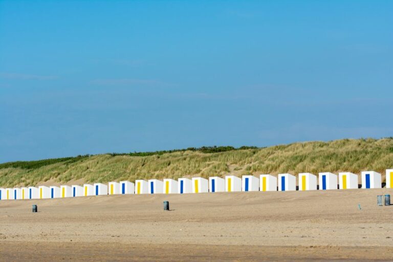 Row of vibrant beach huts against sandy dunes at Cadzand, Netherlands.