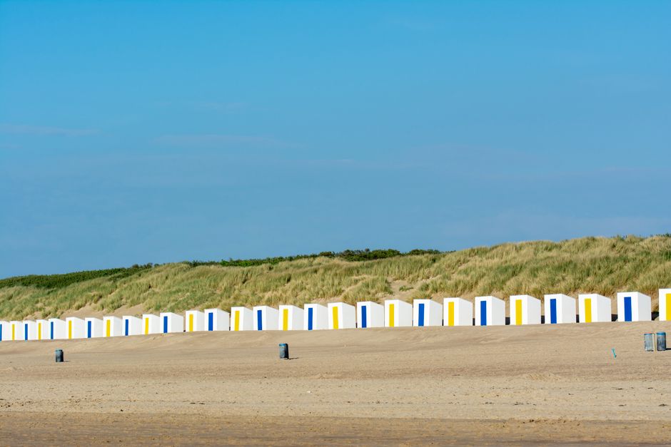 Row of vibrant beach huts against sandy dunes at Cadzand, Netherlands.