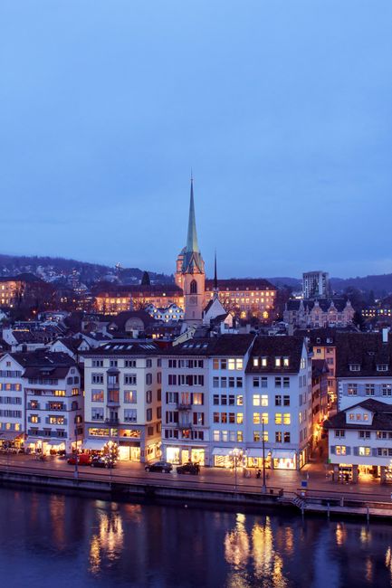 A stunning view of Zurich at dusk featuring illuminated historic buildings and a prominent church spire.